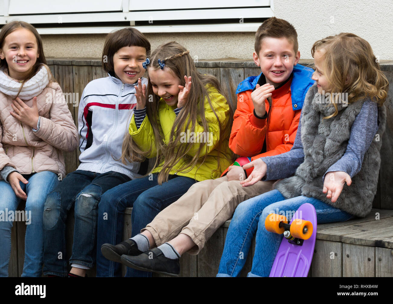 Cheerful kids whispering in other ears in city street Stock Photo
