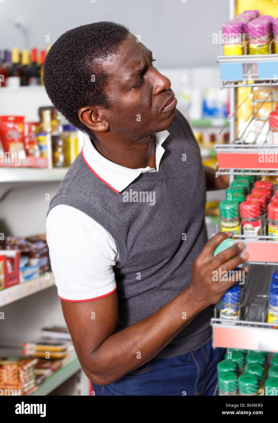 Portrait of upset African man choosing spice from the range in ...