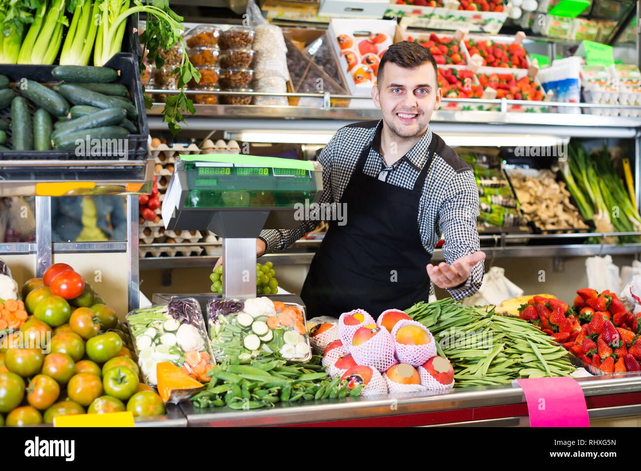 cheerful male seller showing assortment of fruits and vegetables in the ...