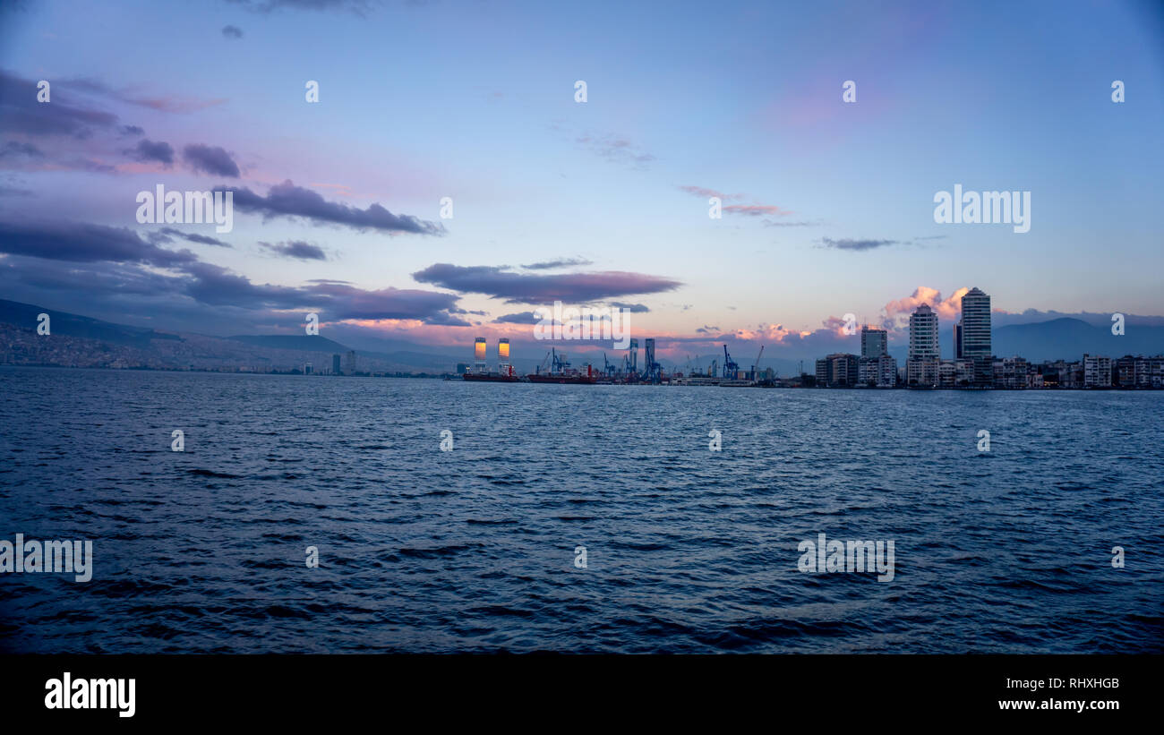 cityscape of the city of Izmir, Turkey, from the aegean sea. View of the skyscraper and the merchant port during the dawn. Sunset reflected in the Stock Photo