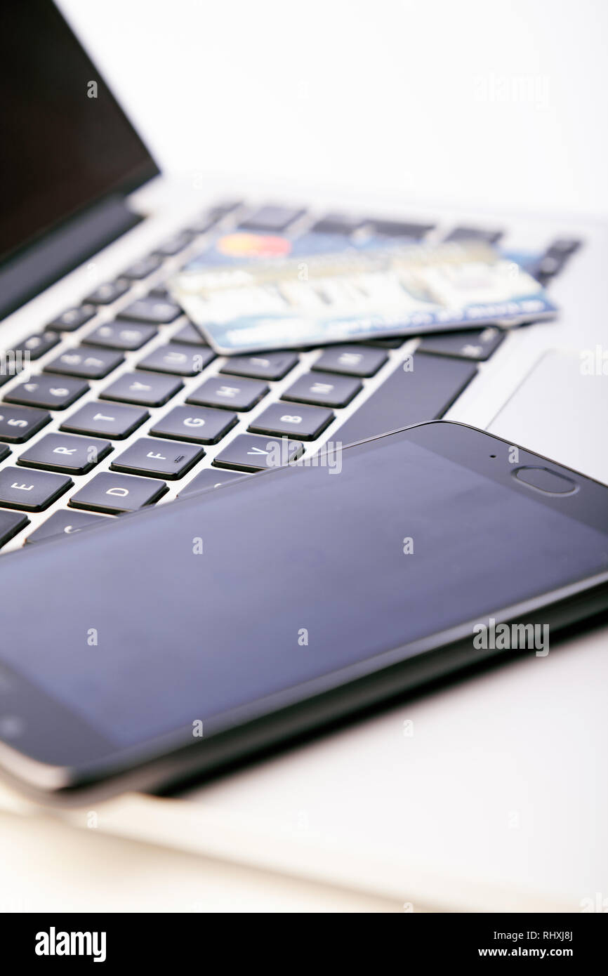 A mobile phone sitting on top of a laptop with credit cards in the background. Stock Photo