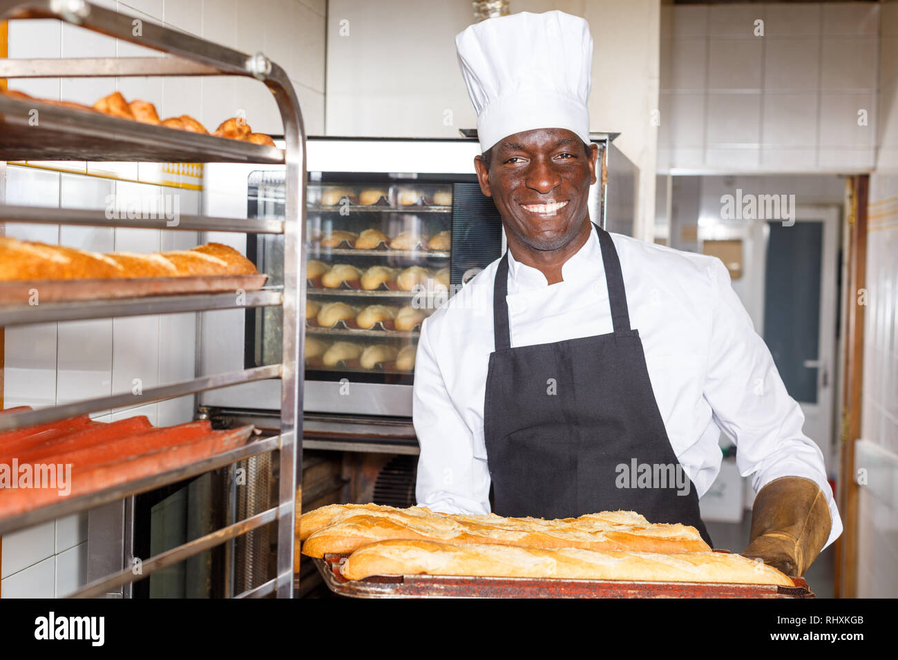 Portrait of African American baker putting fresh baked baguettes on rack at bakery Stock Photo