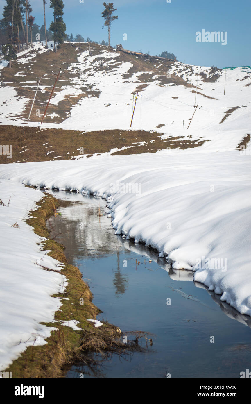 A small narow stream in a snow landscape with a hill in the background Stock Photo