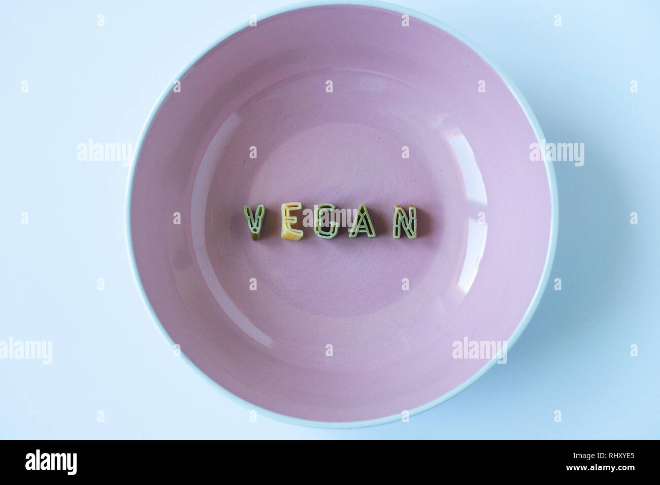 The word 'vegan' written with green pasta letters in a beige dish. Veganism background, conceptual wallpaper. Stock Photo