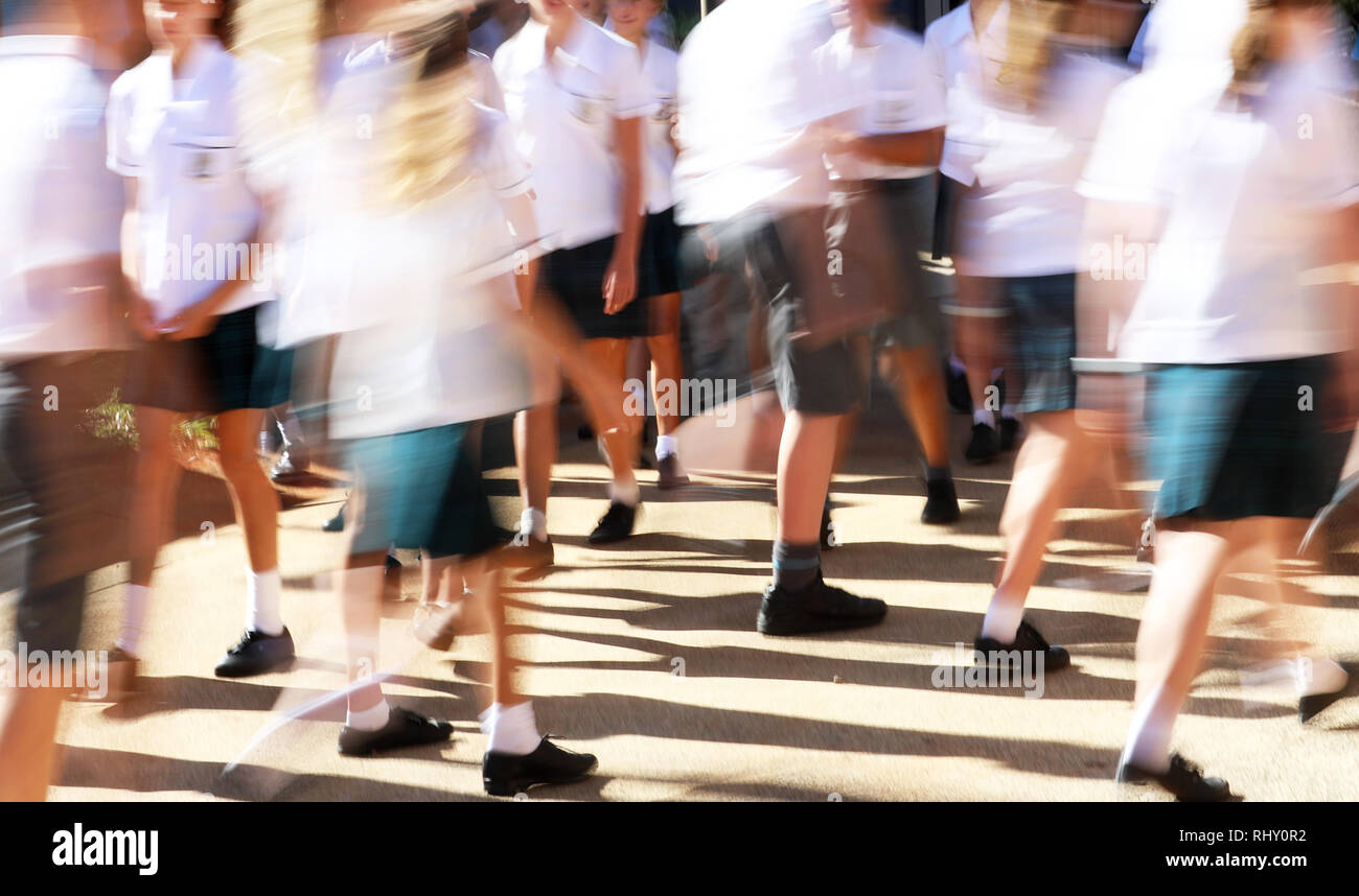 Large number of male and female students wearing neat uniforms moving between classes in a high school yard environment.  heavy motion blur. Stock Photo