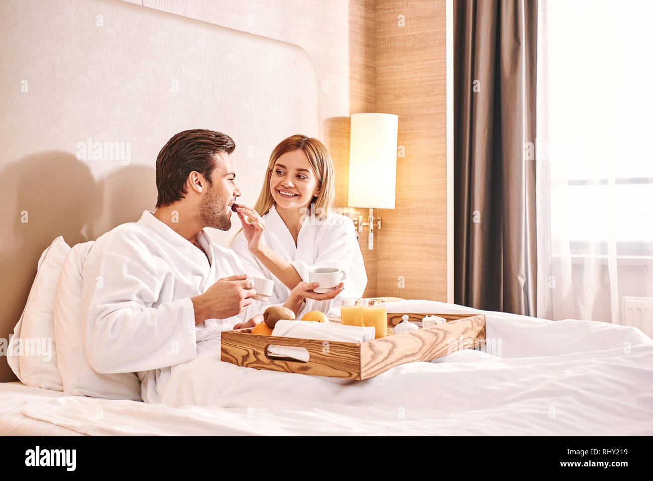 Feeding each other. Couple are eating in hotel room bed together. Love story. Stock Photo