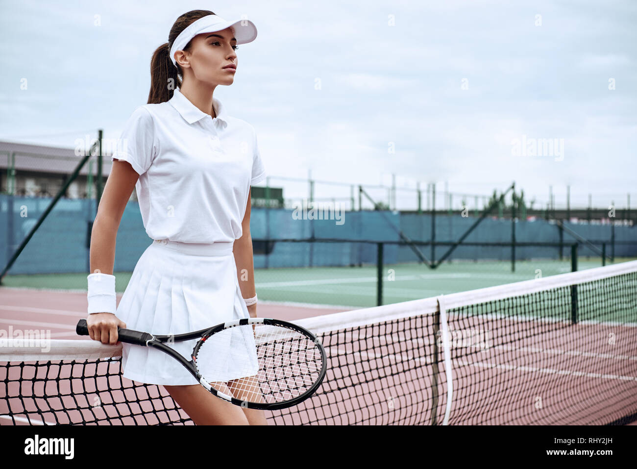 Girl in white sportswear stands on the tennis court near the net