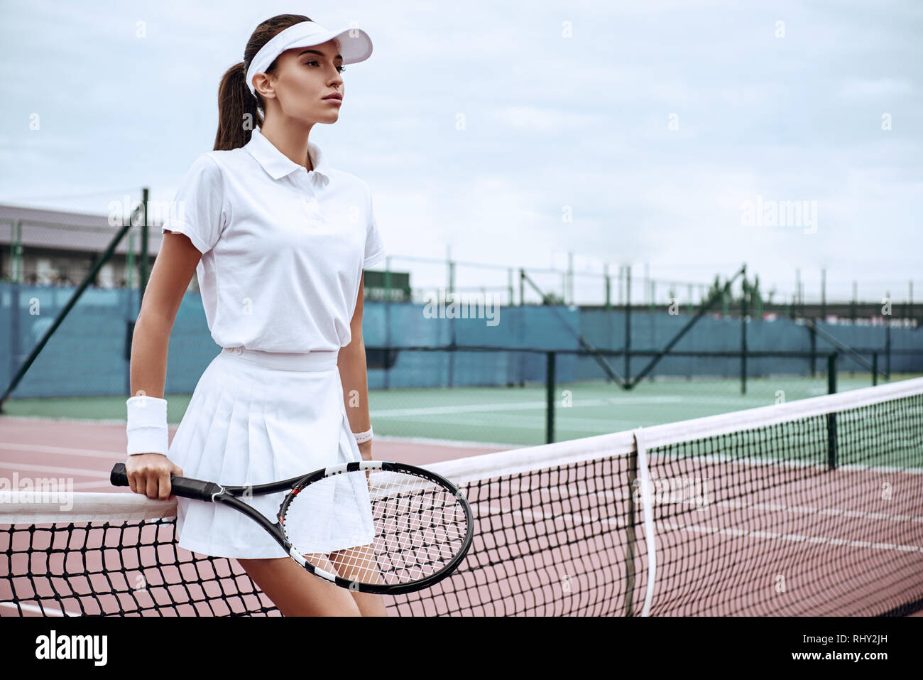 Girl in white sportswear stands on the tennis court near the net looking  away Stock Photo - Alamy