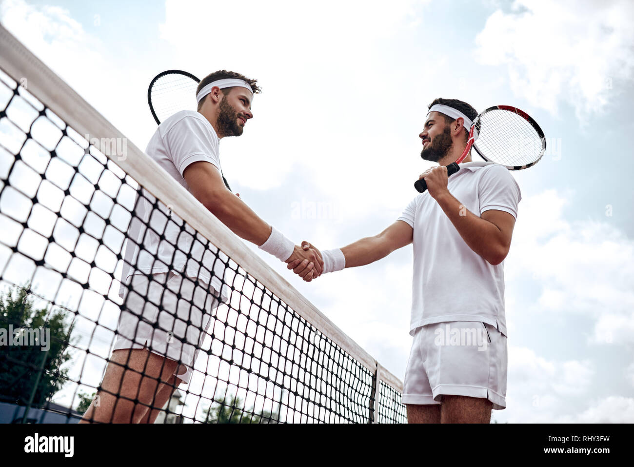 Two handsome tennis players shake hands on the court after the match Stock Photo