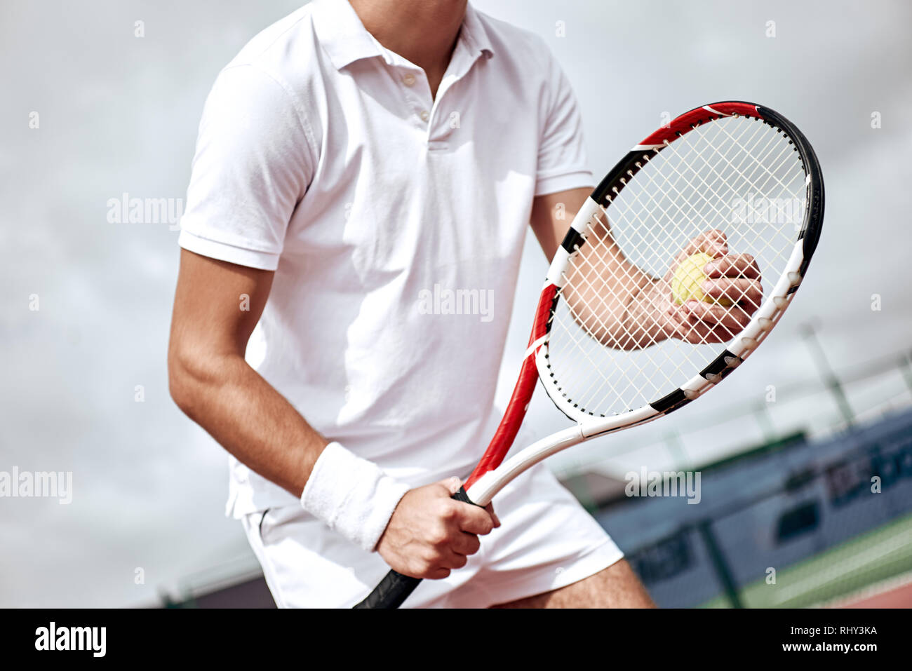 Tennis player in white polo stands on the court with the racket and the ball in his hands Stock Photo
