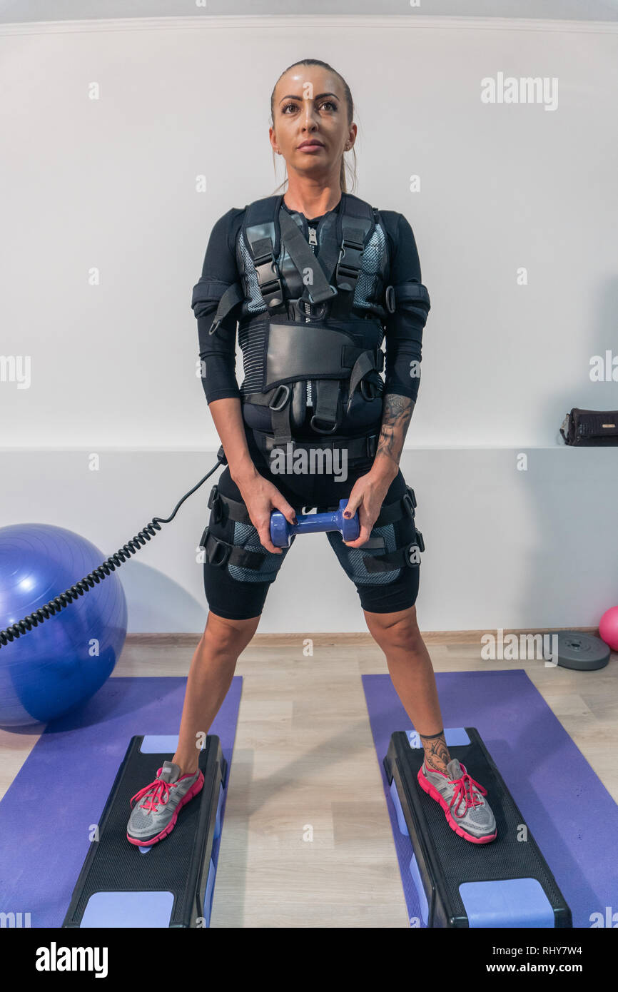 Beautiful athletic girl in an EMS suit does exercises with weight in a  fitness room Stock Photo - Alamy