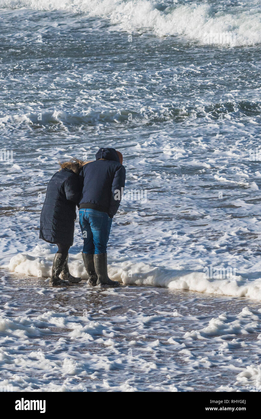 Two people standing in the sea with spume and foam flowing around them. Stock Photo