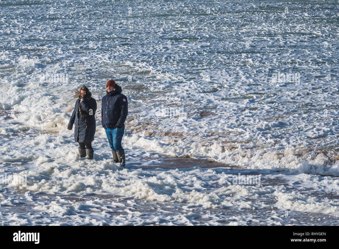 Two people standing in the sea with spume and foam flowing around them. Stock Photo