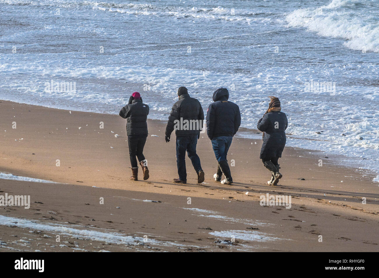 People wrapped up against the cold weather walking along Fistral Beach in windy weather conditions. Stock Photo