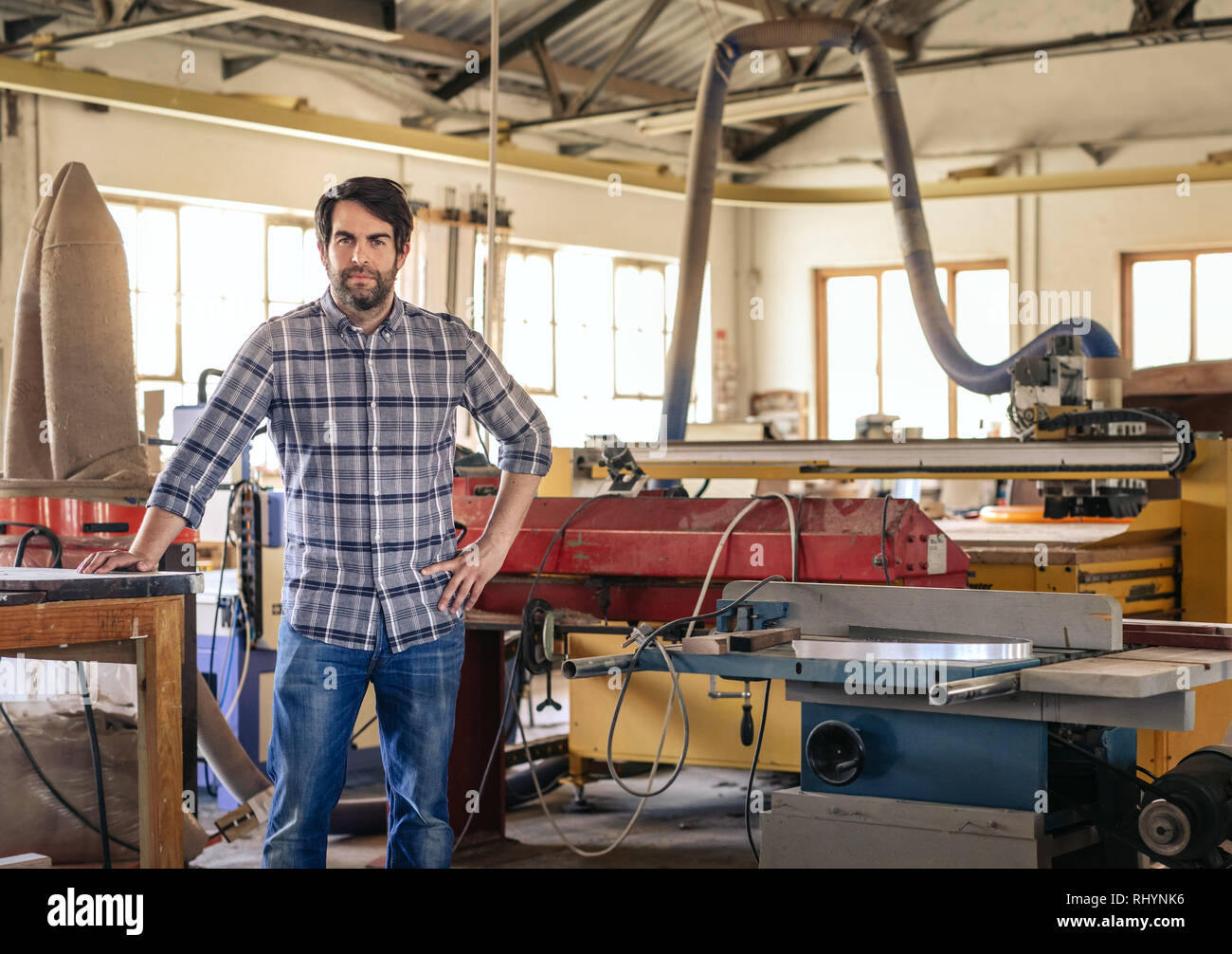 Young entrepreneur leaning on a table in his large workshop Stock Photo