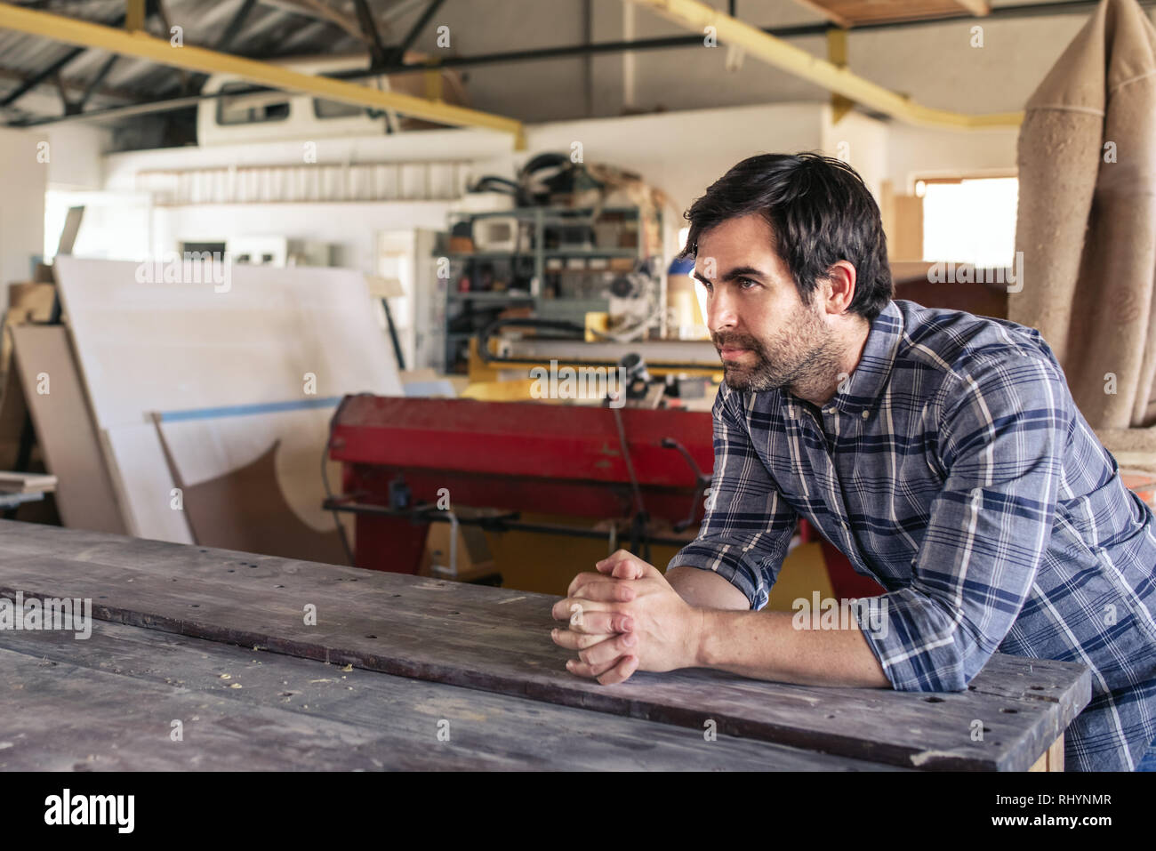 Craftsman leaning on a workshop bench deep in thought Stock Photo