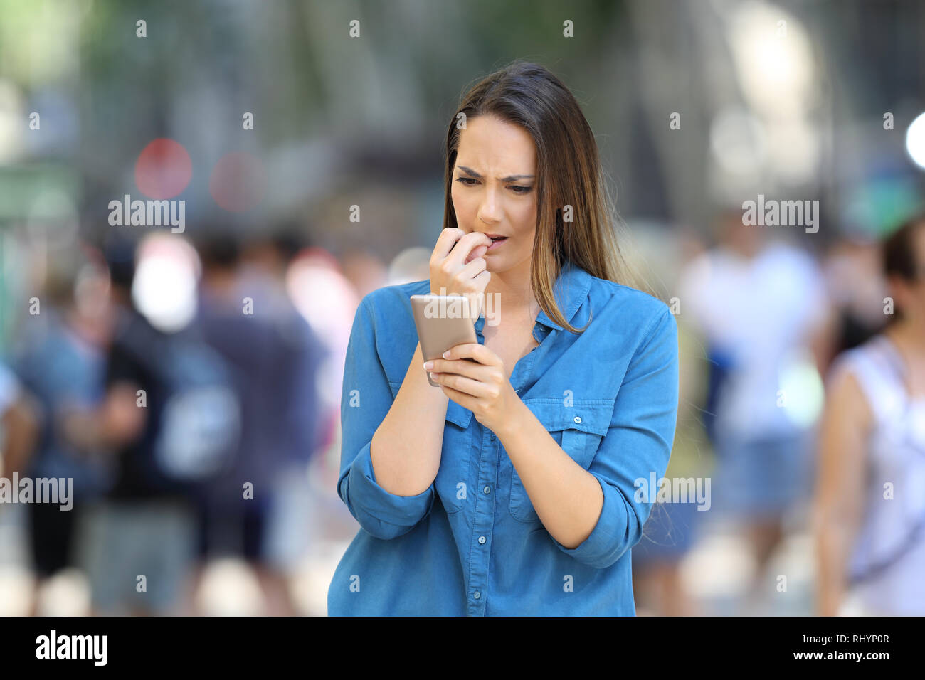 Nervous woman biting nails checking smart phone content standing in the street Stock Photo