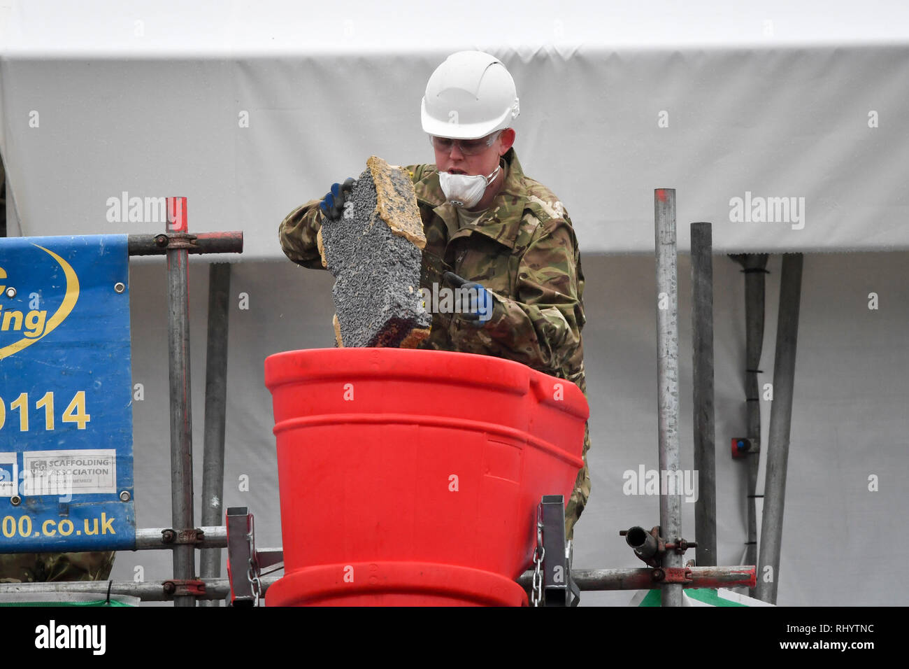 A man dressed in British Army fatigues throws a brick down a chute after it is removed from the Skripals' house in Salisbury, as the roof is being taken down after the novichok attack. Stock Photo