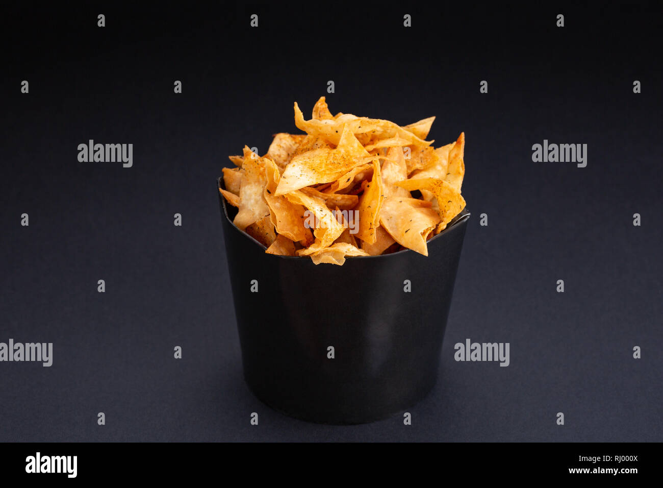 Potato chips in a bowl. A heap of potato crisps piled up in a bowl. The food is sitting on a black background. Stock Photo