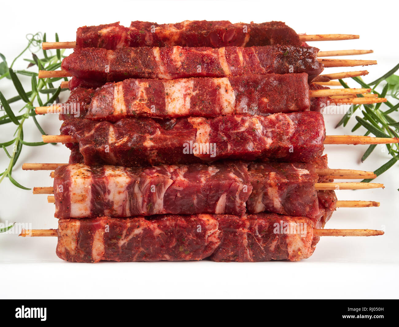 Raw fresh beef and lamb skewers, uncooked, on a white plate, garnished with fresh pea shoots and rosemary sprigs Stock Photo