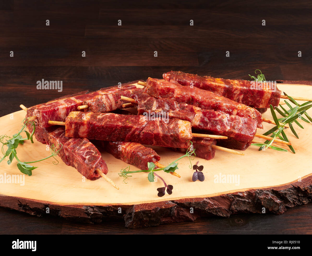 Raw fresh beef and lamb skewers, uncooked, on a wood board, garnished with fresh pea shoots and rosemary sprigs Stock Photo