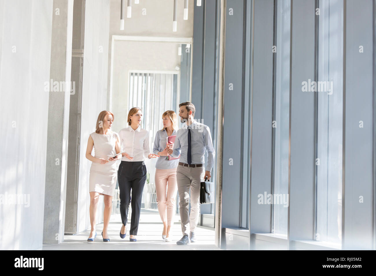 Professionals communicating while walking in office corridor Stock Photo