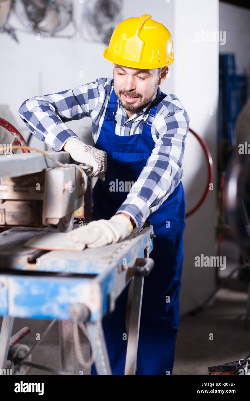 Male is using disk saw to cut tile at workshop. Stock Photo