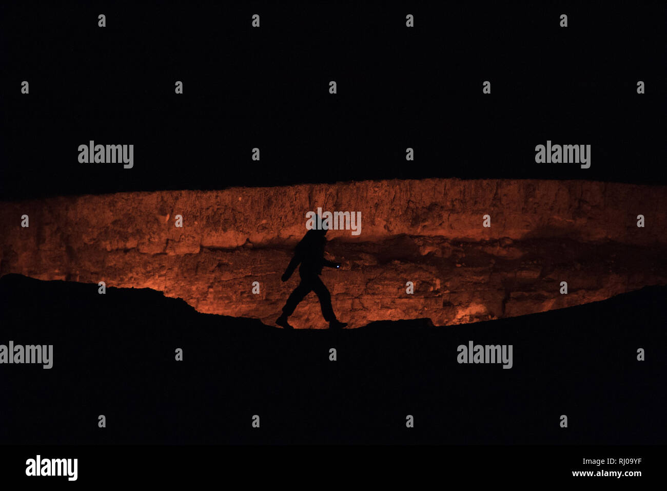 A person silhouetted walking along the rim of The Darvasa Crater, also known as the Doorway to Hell, the flaming gas crater in Turkmenistan Stock Photo