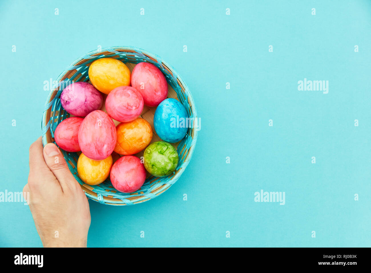 Hand holds colorfully painted easter eggs in the basket for easter Stock Photo