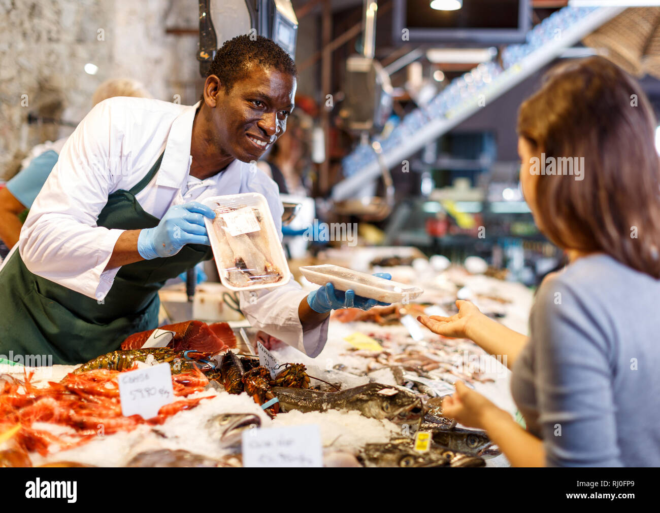 Portrait of salesman in apron offering female customer fresh fish at  seafood shop Stock Photo - Alamy