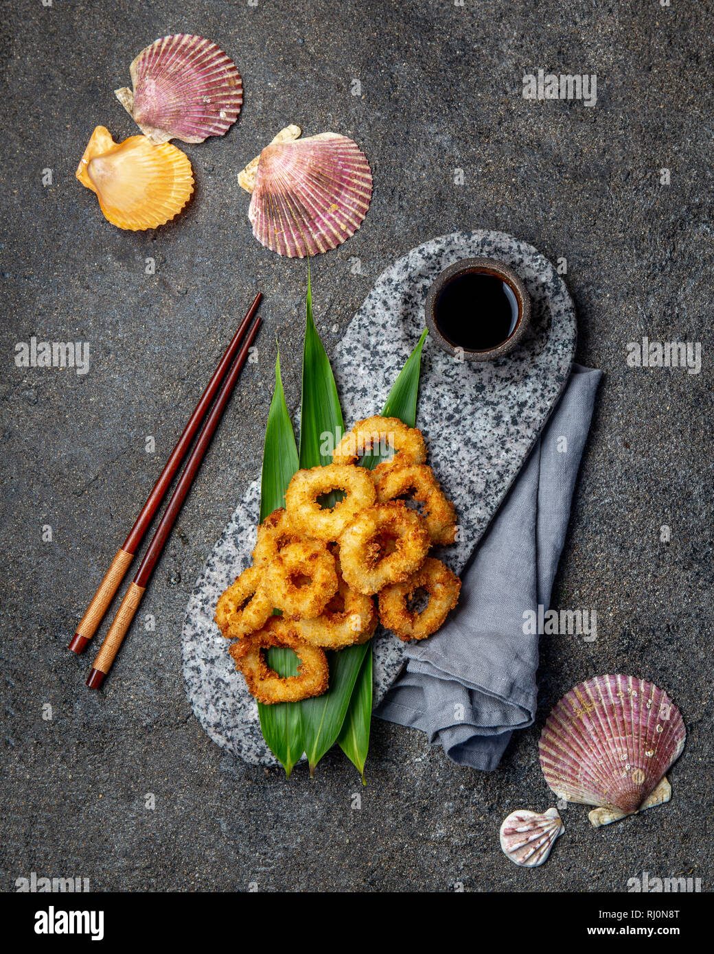 Fried squid rings on stone plate decorated with tropical leaves. Asian food concept, soy sauce and chopsticks Stock Photo