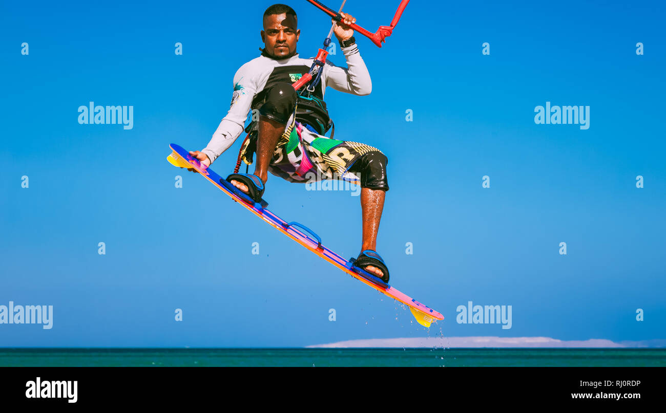 Egypt, Hurghada - 30 November, 2017: Close-up kitesurfer on the surfboard holding the kite stripes. The soaring flight in the blue sky over the Red sea surface. Extreme sport activity. Stock Photo
