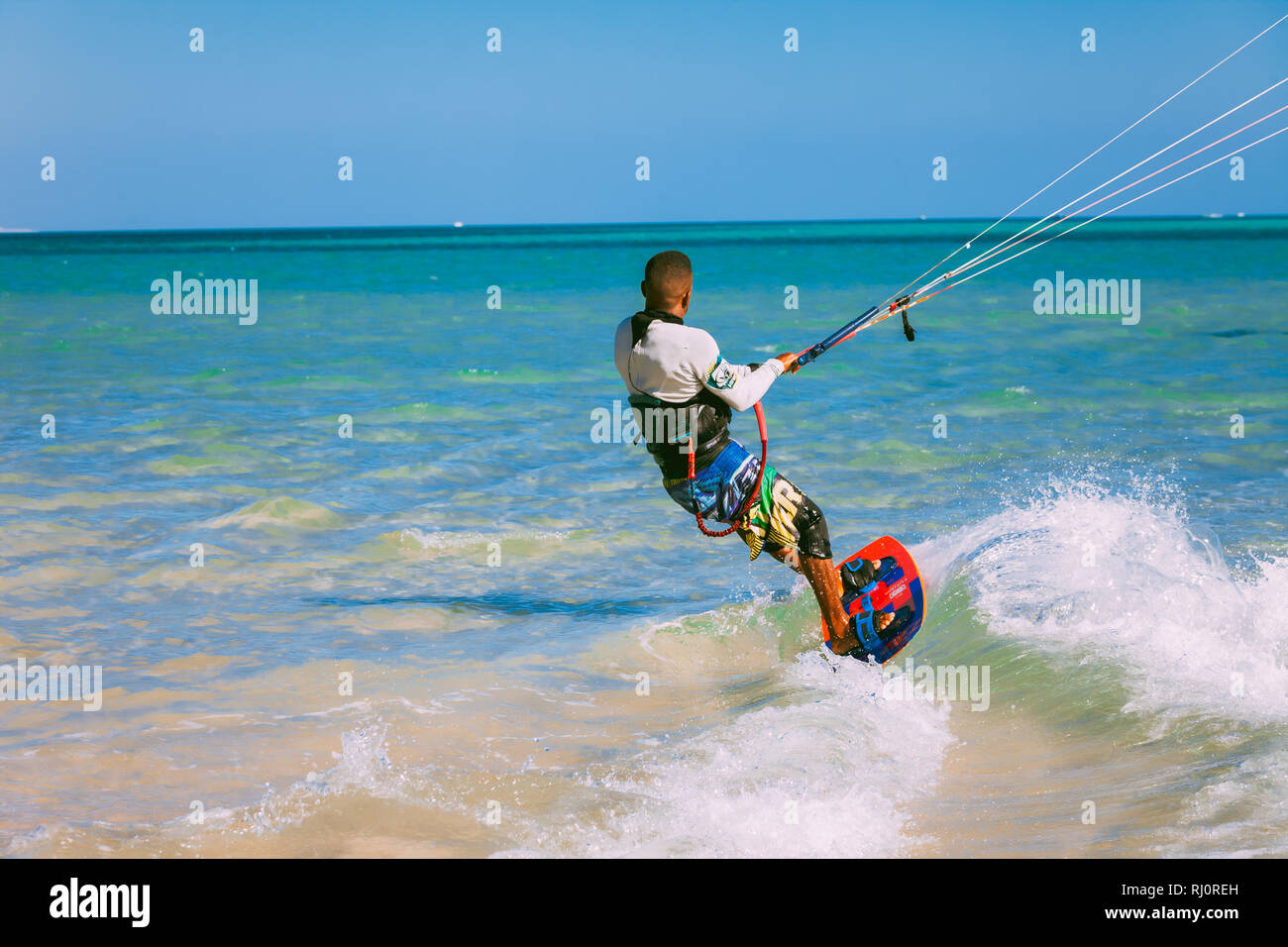 Egypt, Hurghada - 30 November, 2017: Close-up rear view of the surfer on the surfboard holding the kite straps. The wave riding over the crystal clear Red sea surface. Overwhelming marine landscape. Stock Photo