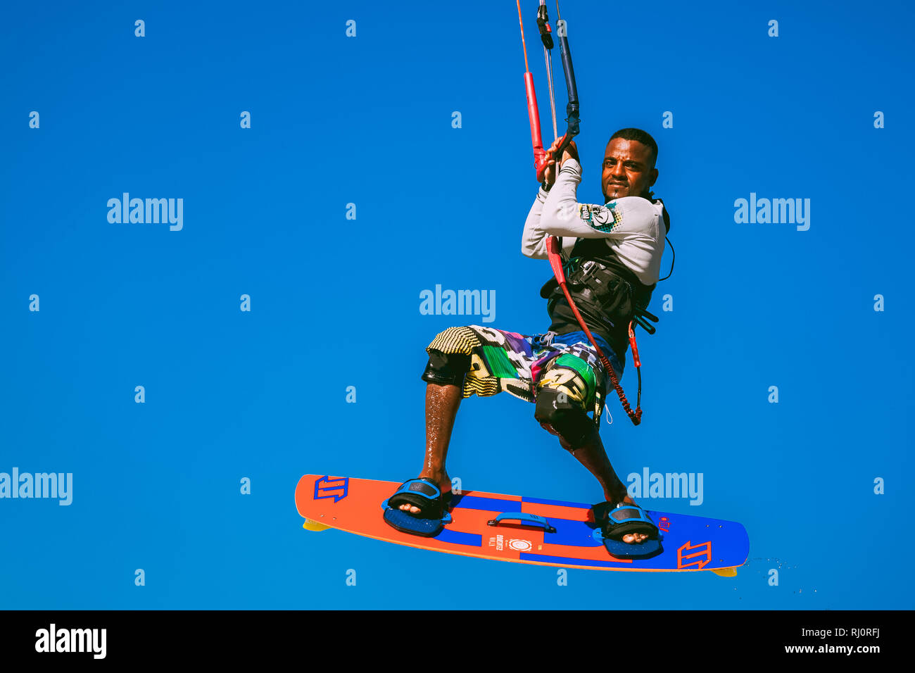 Egypt, Hurghada - 30 November, 2017: Close-up sportsman kitesurfer soaring in the blue sky. The surfer fully equipped with the board and kite elements in the air. The extreme professional flight. Stock Photo