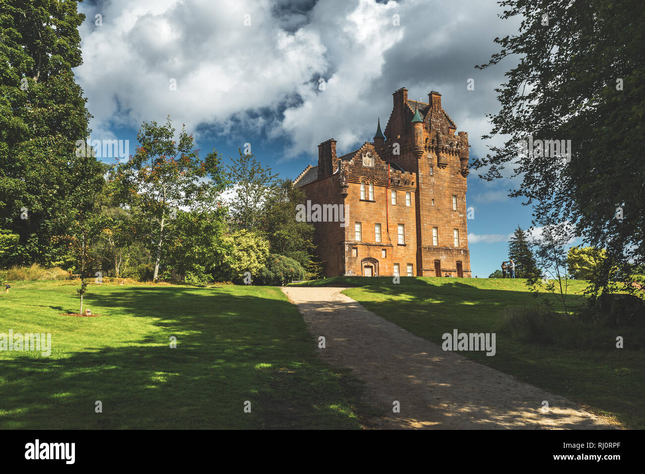 Path to the ancient castle. Northern Ireland. Picturesque scene the vintage building surrounded by the green lawn and trees. Blue cloudy sky background. Stunning Irish landscape. Historical house. Stock Photo