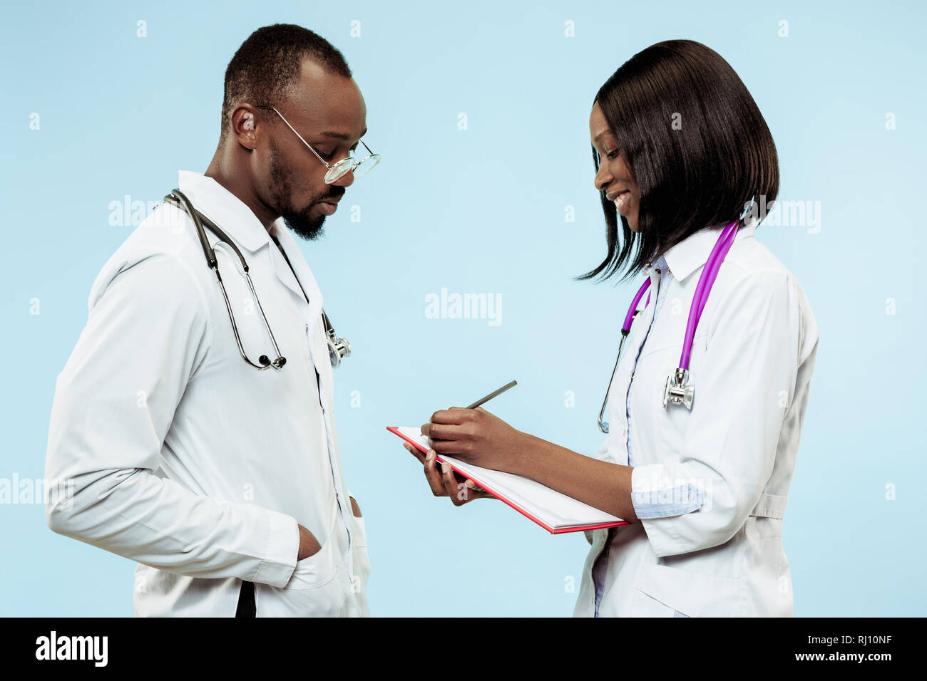 The female and male smiling happy afro american doctors on blue background at studio.The clinic, medical, nurse, health, healthcare, hospital, care, job, professional concept Stock Photo