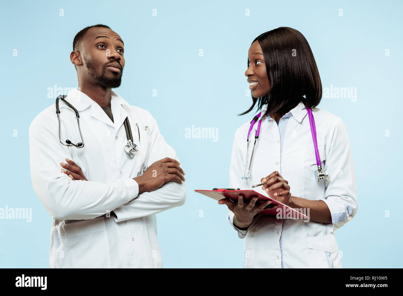 The female and male smiling happy afro american doctors on blue background at studio.The clinic, medical, nurse, health, healthcare, hospital, care, job, professional concept Stock Photo