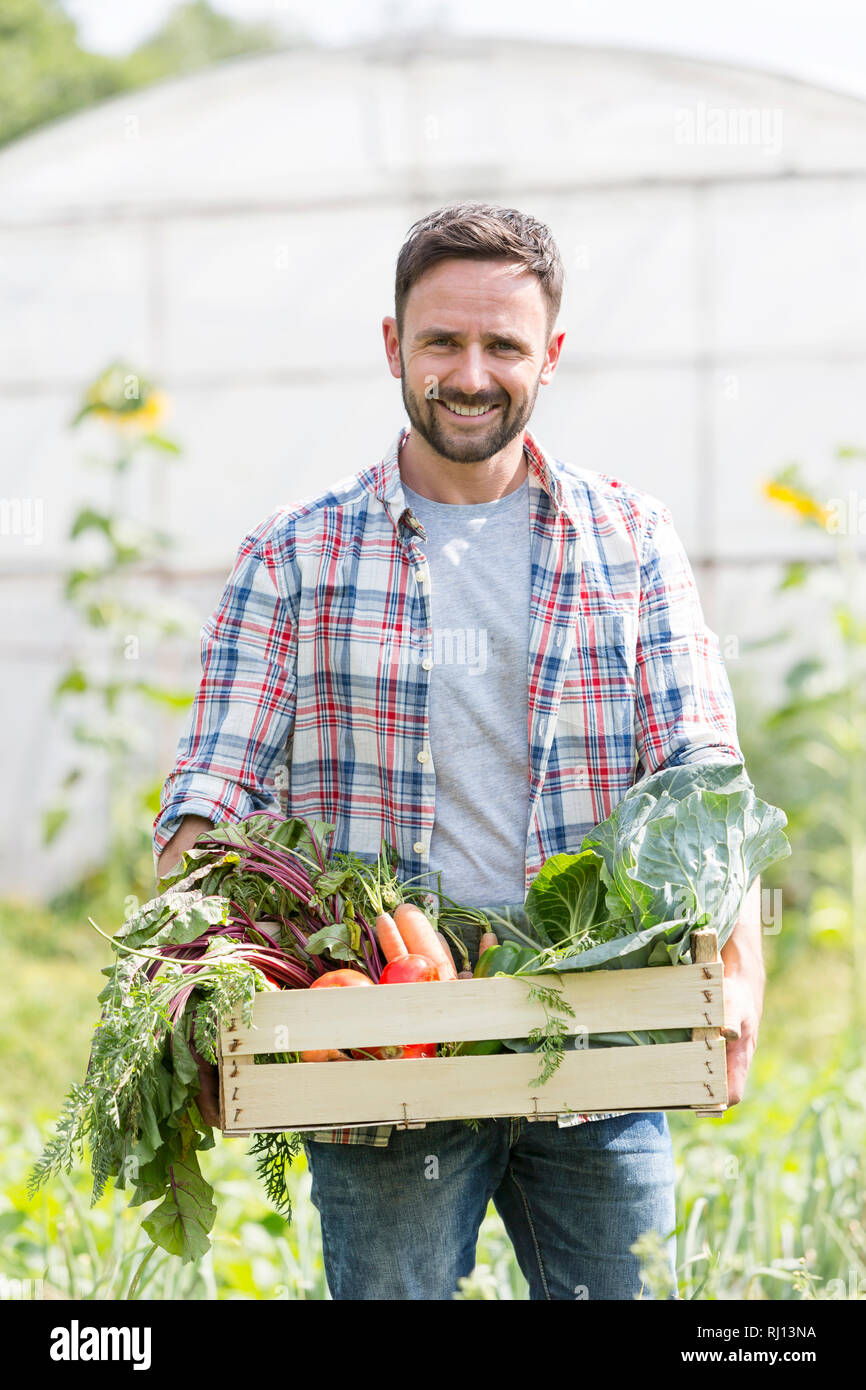 Portrait of smiling farmer carrying vegetables in crate at farm Stock ...