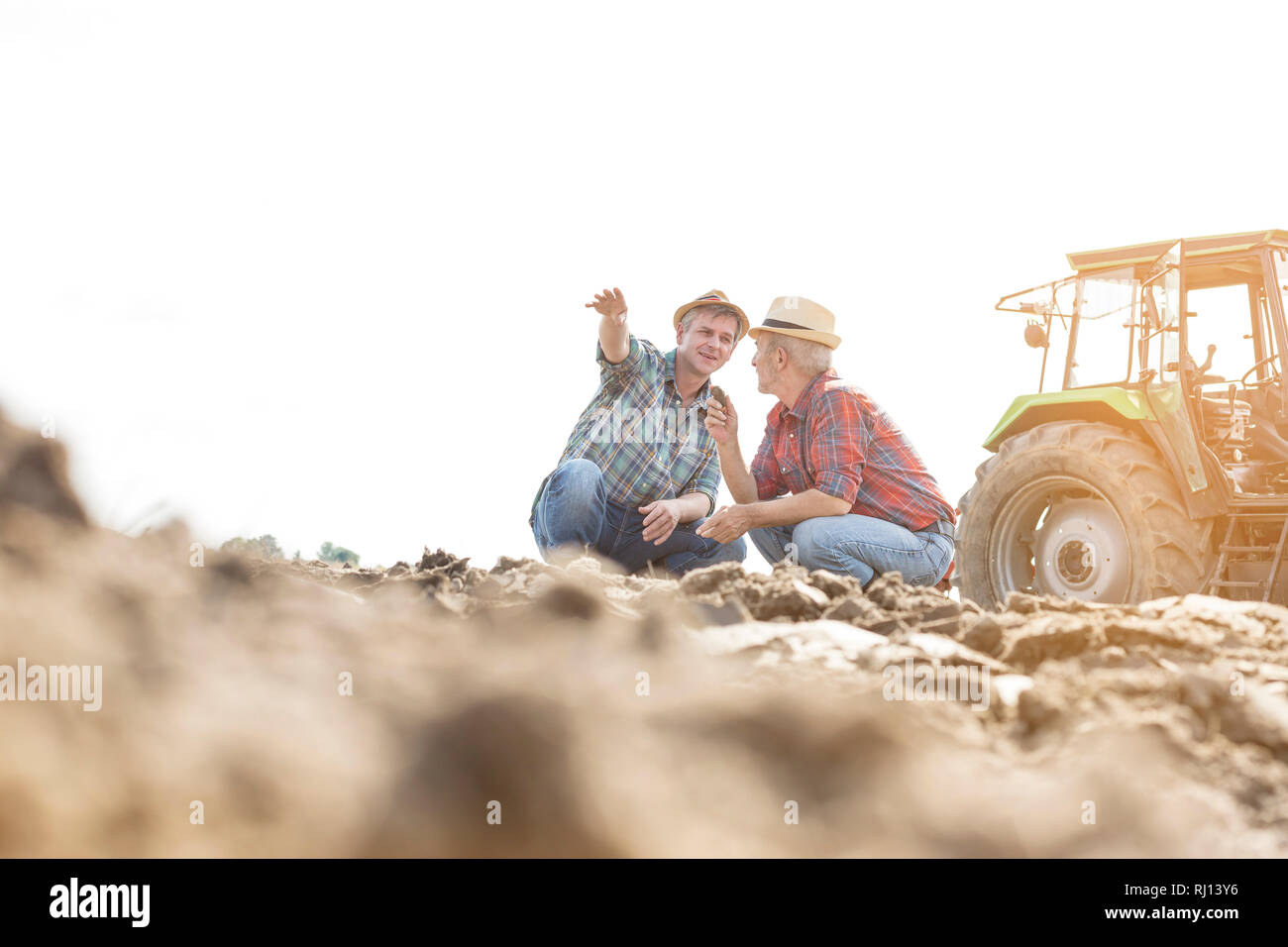 Farmers discussing while crouching on field at farm Stock Photo