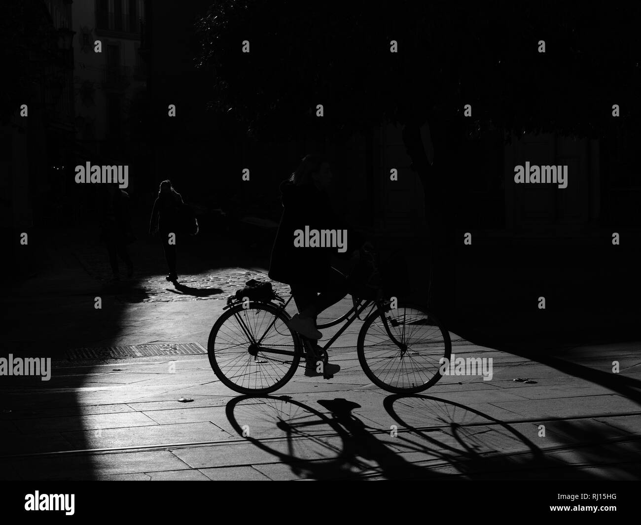 Strong Graphic Shadow Silhouettes of cyclists on bikes in pool of sunlight on street Seville Spain Stock Photo