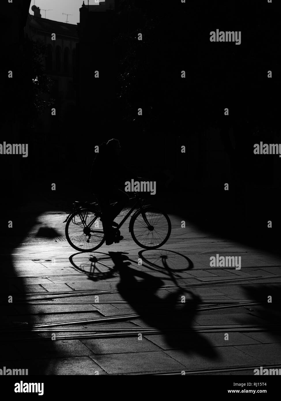 Strong Graphic Shadow Silhouettes of cyclists on bikes in pool of sunlight on street Seville Spain Stock Photo