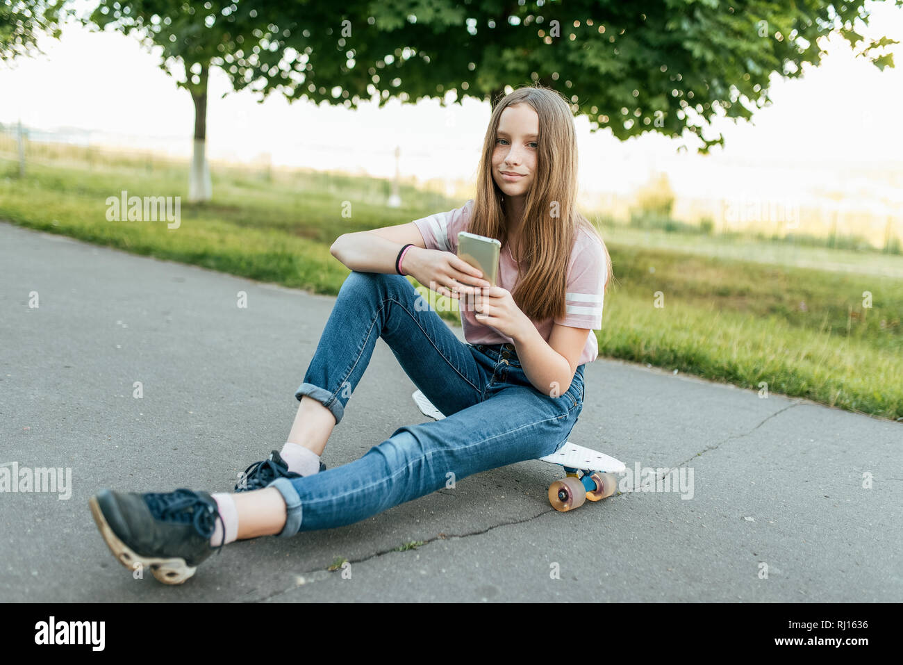 Girl teenager 9-11 years old, sits on board in hands of phone. In summer in  city in casual jeans and a pink T-shirt. Communication in the Internet, in  Stock Photo - Alamy