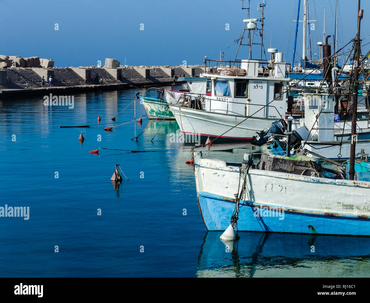 Number of small fishing sail boats, floating on smooth blue sea water at Jaffa port harbor in Israel, on a beautiful sunny summer day. Stock Photo
