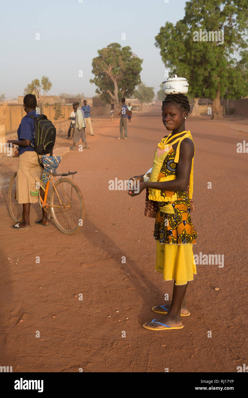Yako town, Burkina Faso; A girl on her way to school in the early morning, with her lunch in a pot on her head. Stock Photo