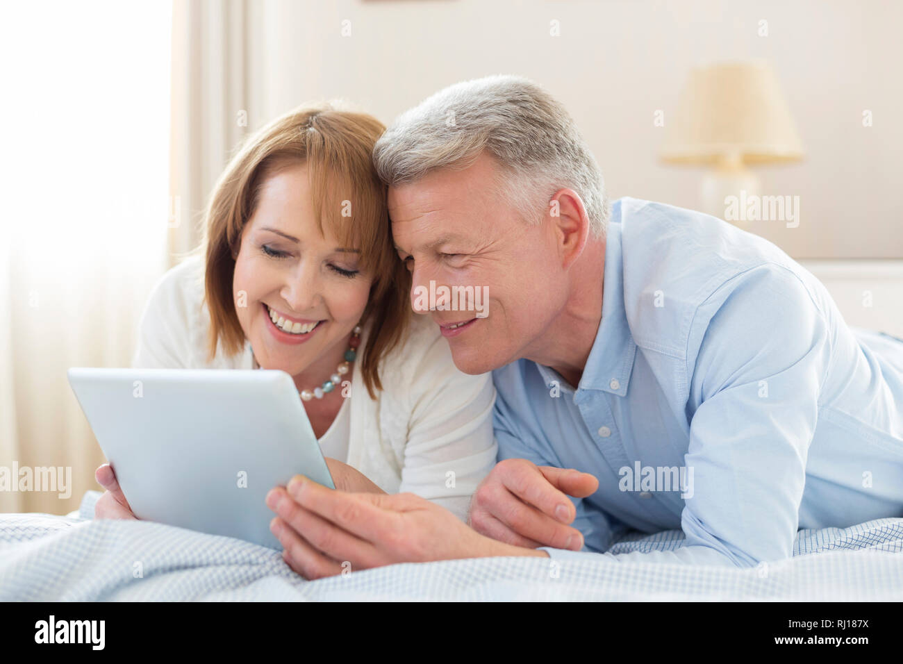 Smiling mature couple sharing digital tablet while lying on bed at home Stock Photo