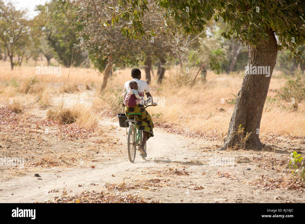 Samba village, Yako Province, Burkina Faso : Collette Guiguemde, 26 with her baby Ornela Divine Zoundi, 18 months, cycles home from her husband's market garden with the ocra she has just harvested. Stock Photo