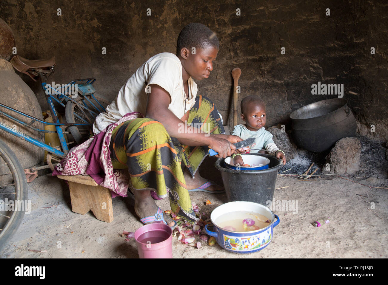 Samba village, Yako Province, Burkina Faso : Collette Guiguemde, 26 with her baby Ornela Divine Zoundi, 18 months, cooks a meal for her children and her parents-in-law with the okra she has just harvested, and makes a sorghum porridge or Tao. Stock Photo