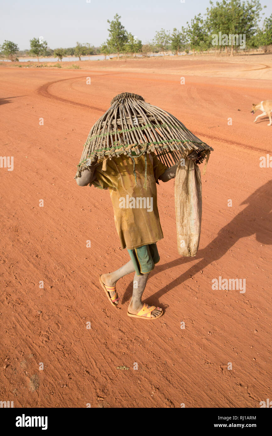 Samba village, Yako Province, Burkina Faso: A young boy carryng a fishing basket to catch fish in the lake on one of the days when fishing is allowed. Stock Photo