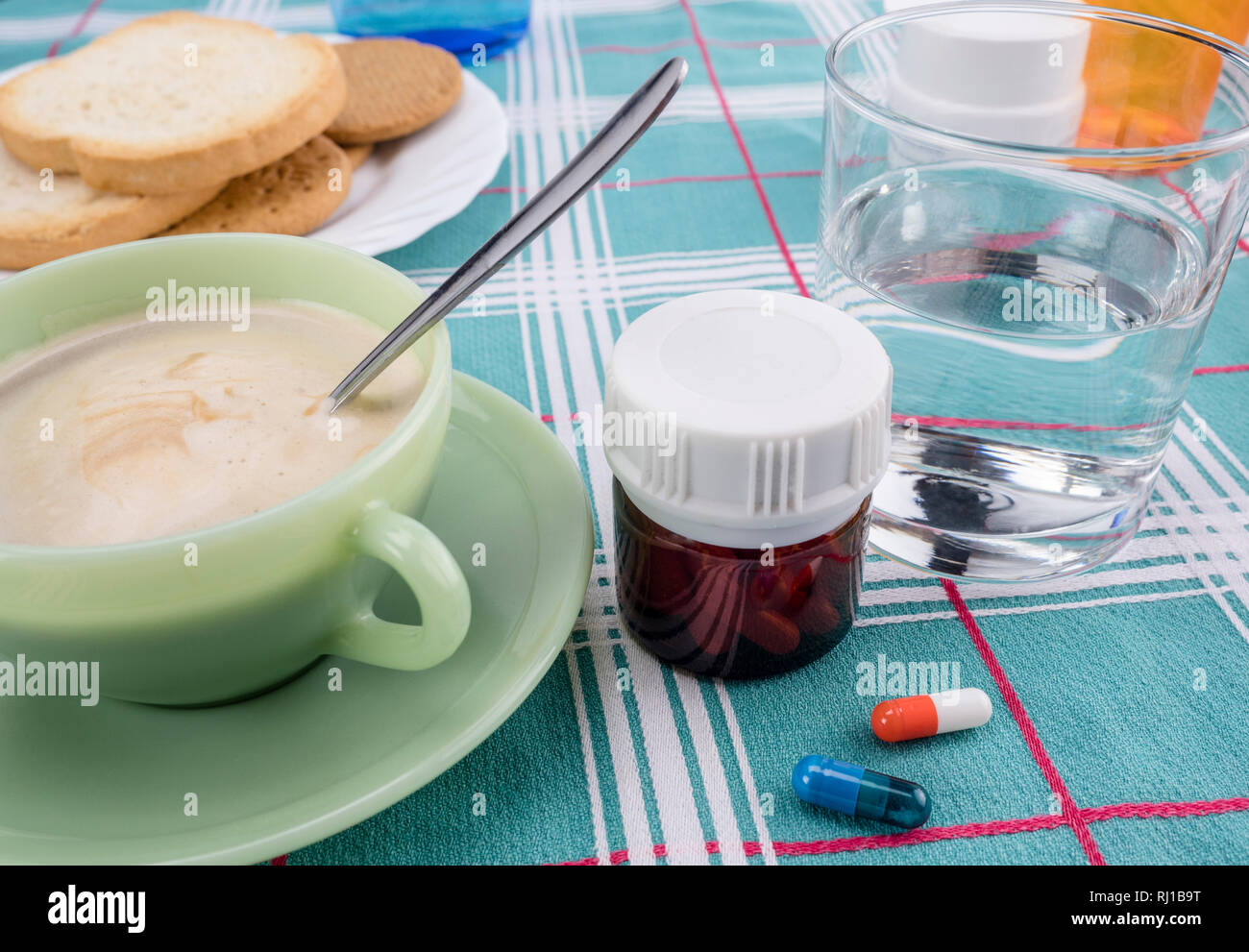 Medication during breakfast, capsules next to a glass of water, conceptual image, horizontal composition Stock Photo