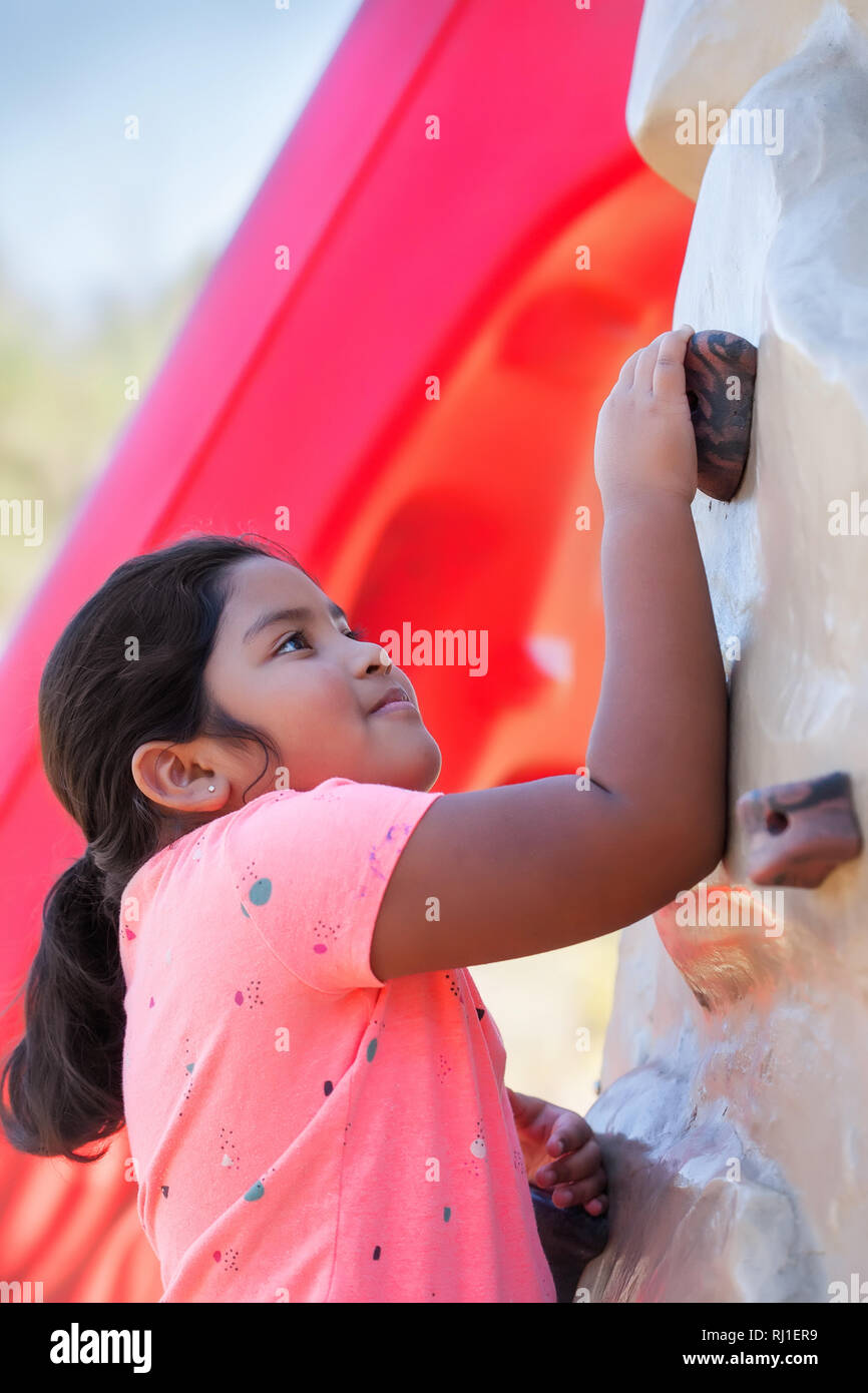 Pre teen girl with a strong arm is holding on to a grip on a rock climbing wall. Stock Photo
